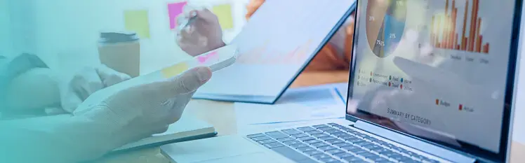 Hands holding a mobile phone in front of a laptop displaying graphics and analytics about their business.